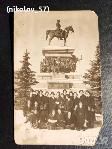 На преден план на старата фотография се вижда група млади жени, позициониращи пред Паметника на...