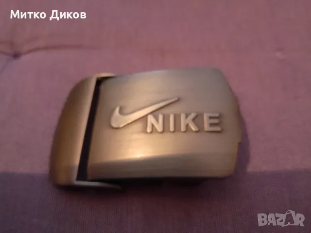 метална катарама тока за колан на марката Nike (типа клипс/плочка със Swoosh лого и надпис Nike).